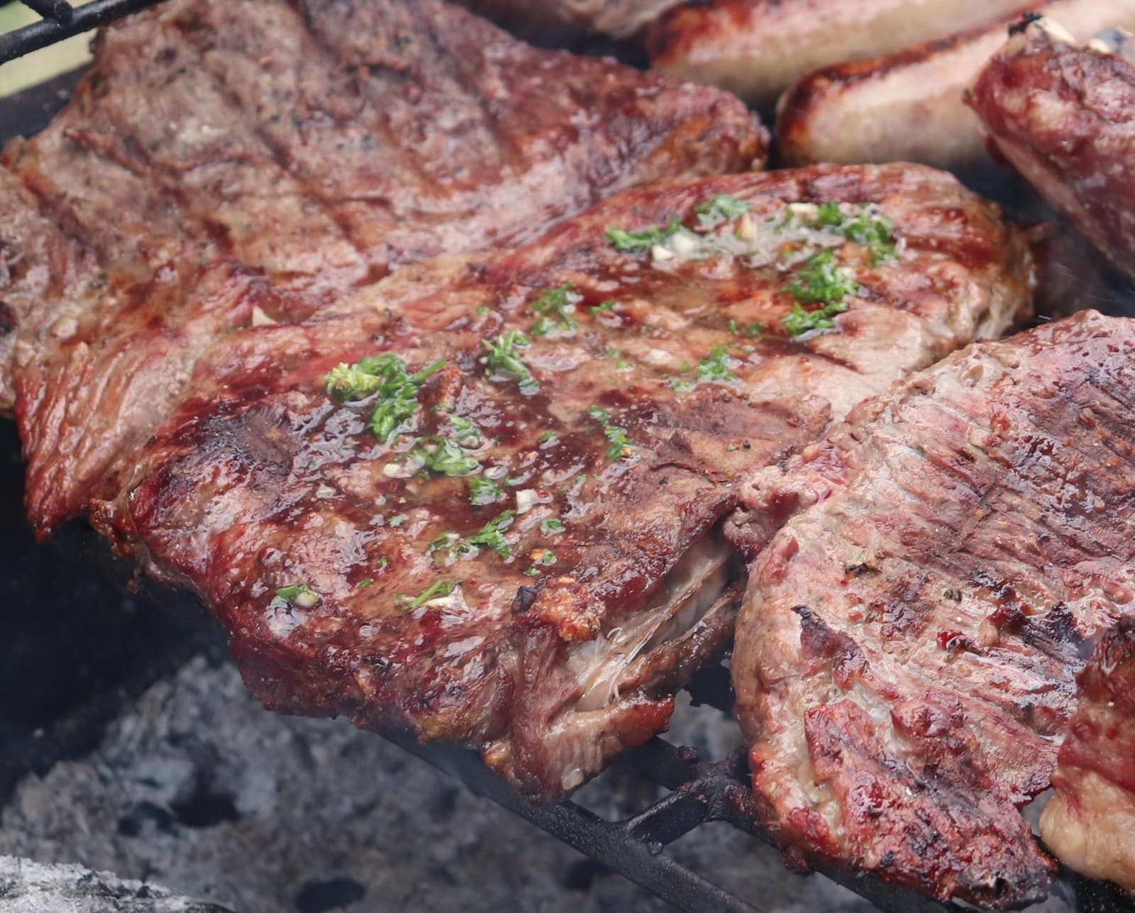 Cuts of meat on the grill with fresh chimichurri, over charcoal embers